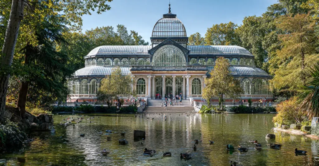 Glass and iron Crystal Palace inside Retiro Park surrounded by trees and a small lake with ducks
