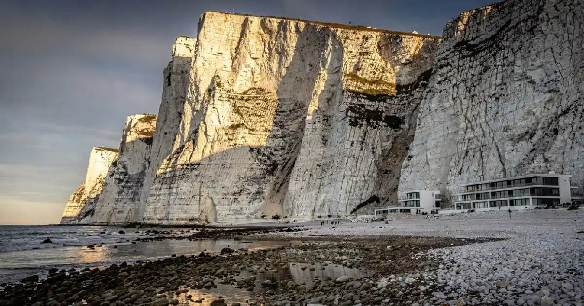 White limestone cliffs rising sharply behind a pebbly beach at Torre del Barone Sciacca Italy with resort nearby.