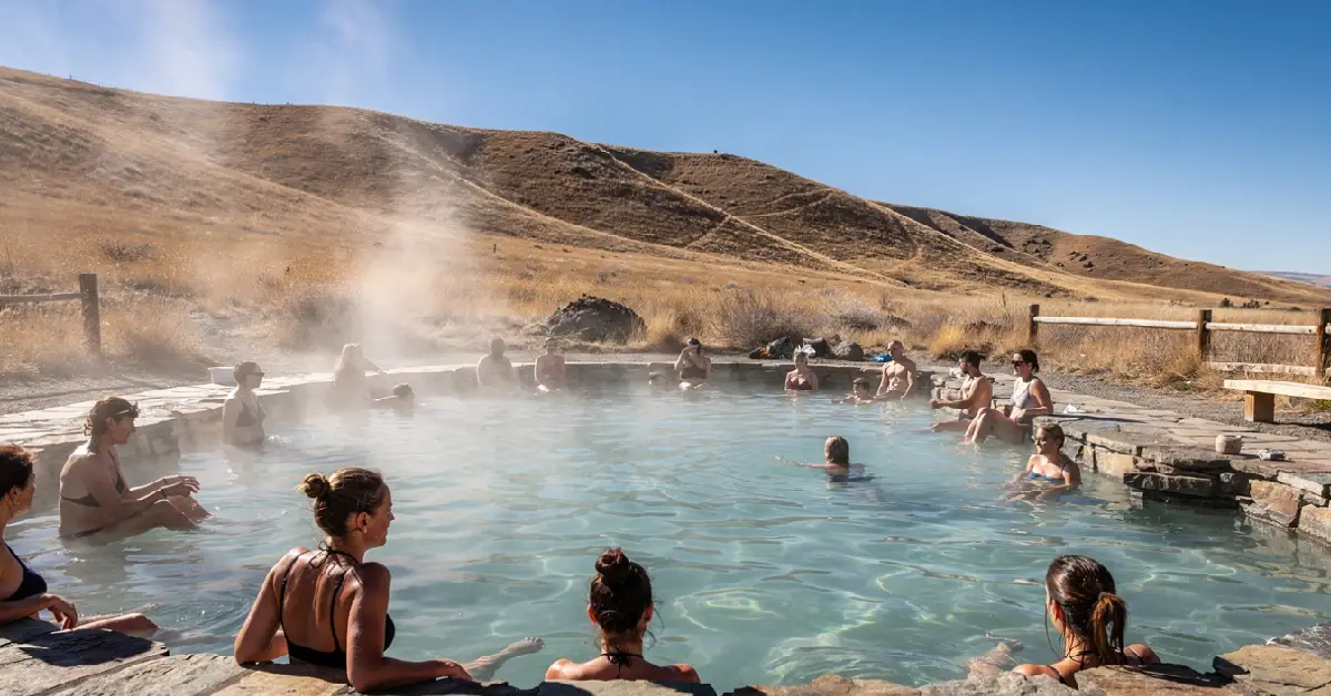 Open natural geothermal soaking pond at Crystal Crane Hot Springs with people relaxing in the water and mountains in the background.